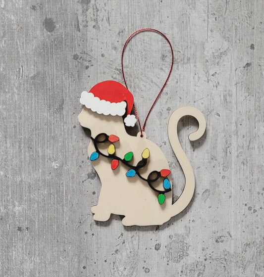 Decorative Christmas ornament shaped like a cat with a Santa hat and string of lights on a gray background.