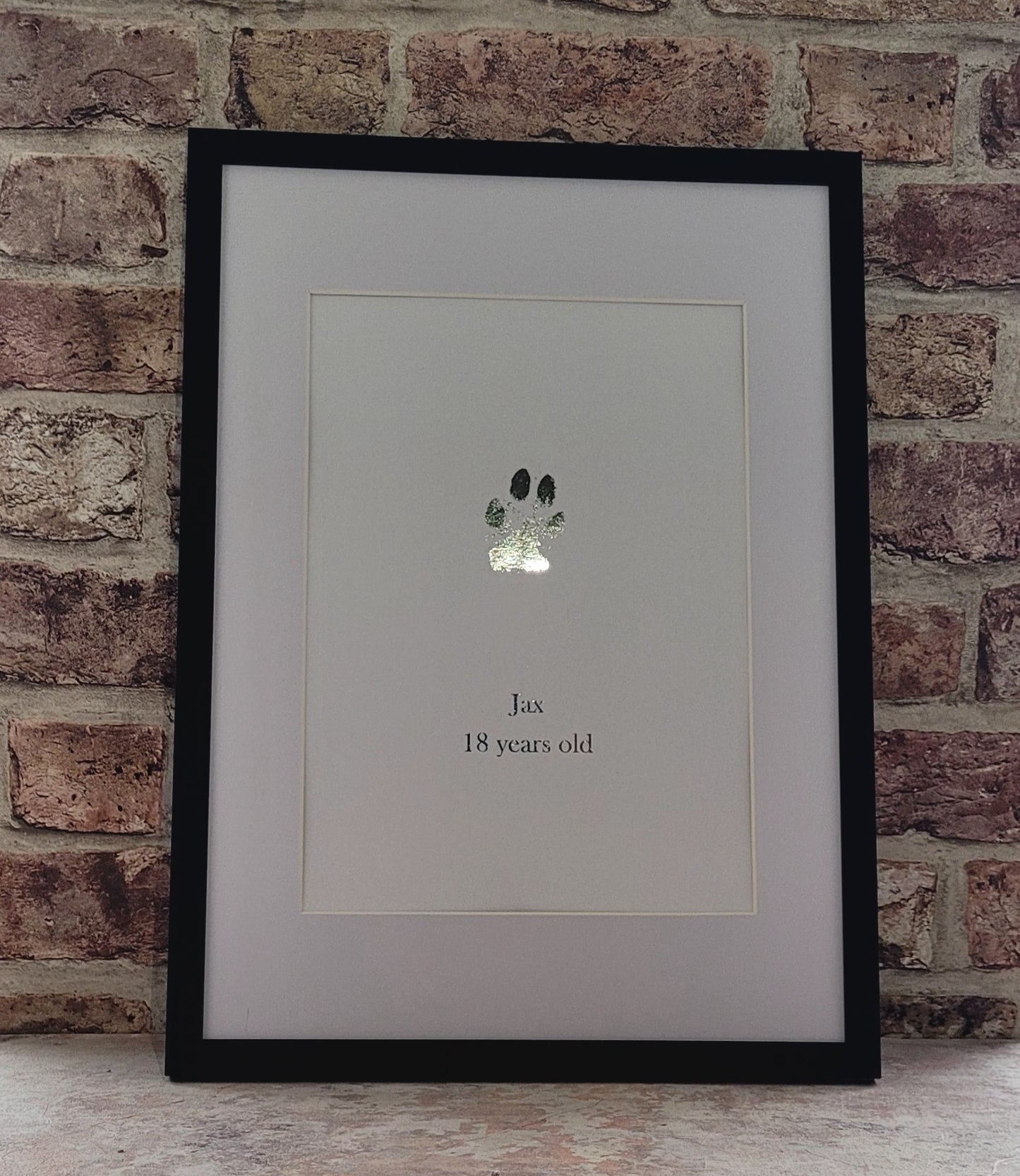 Personalised frame paw print on white card printed in silver foil in black acrylic frame behind glass