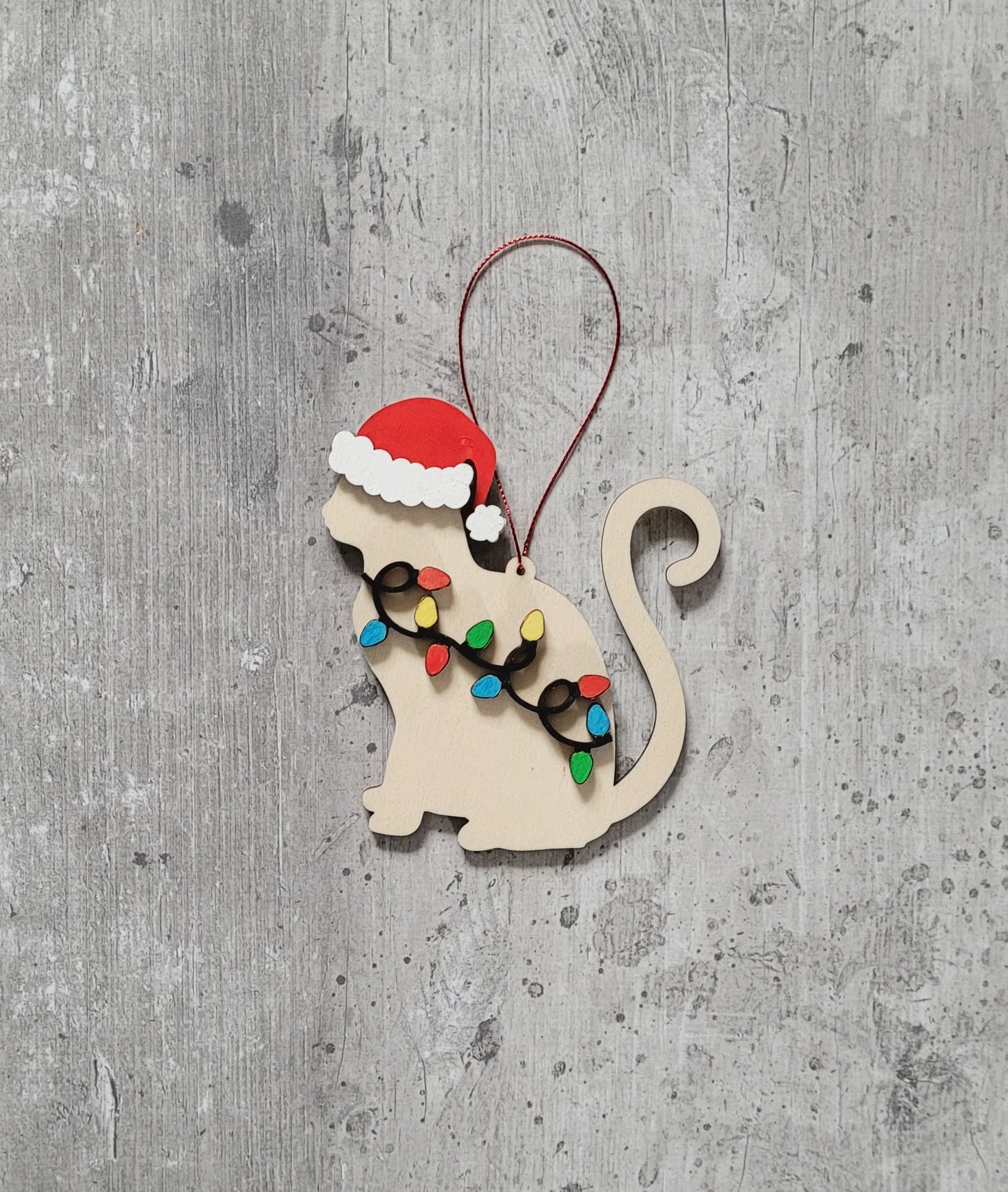 Wooden cat-shaped ornament with Santa hat and Christmas lights on a gray textured background