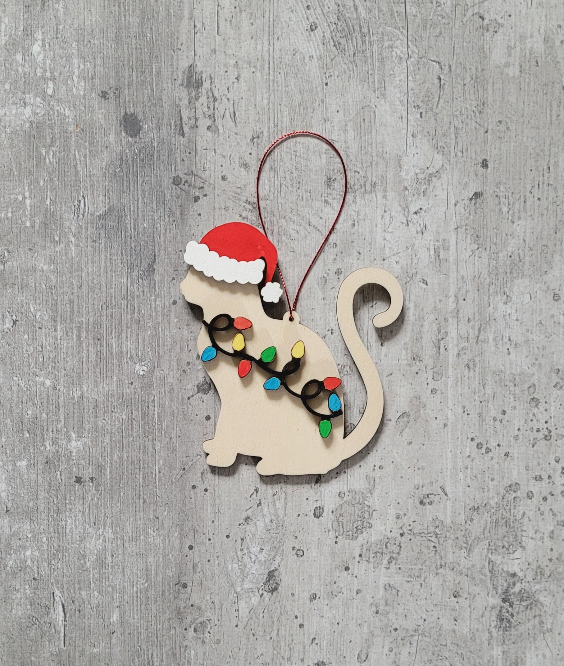 Wooden cat-shaped ornament with Santa hat and Christmas lights on a gray textured background