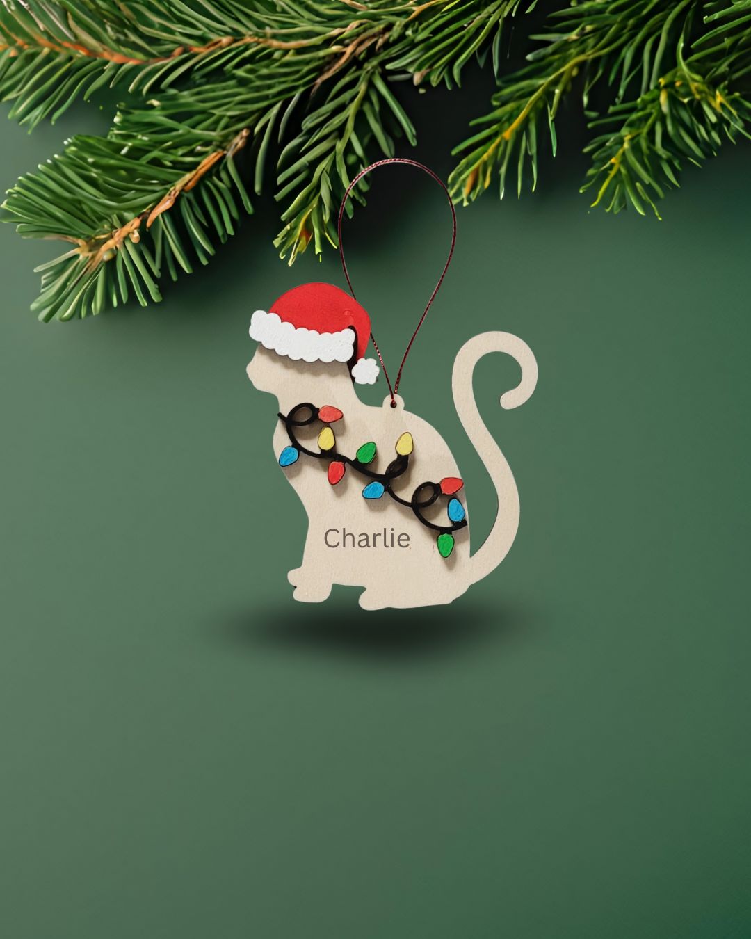 Cat-shaped Christmas ornament with Santa hat and string of lights on a green background