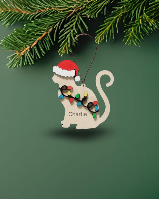 Cat-shaped Christmas ornament with Santa hat and string of lights on a green background