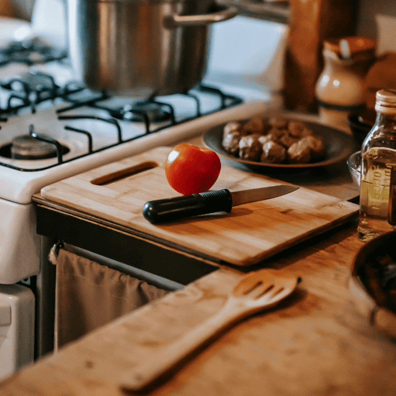 kitchen counter with wooden chopping board with a tomato and knife next to a gas stove 