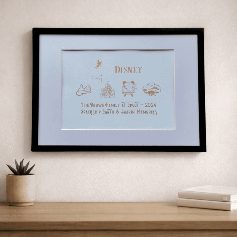magic memories Disney theme a3 print black framed foil colours family personalised print on cream wall and wood shelf detail.
