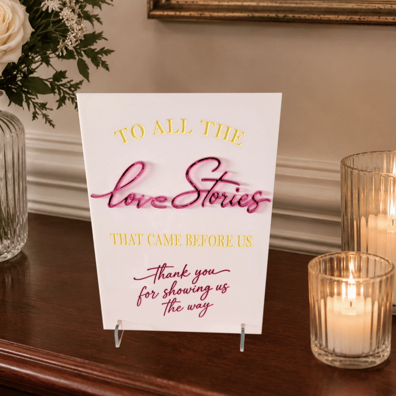 Luxury personalised A5 acrylic wedding Love Stories sign with raised mirrored acrylic lettering, engraved hand-painted details and clear acrylic display feet.